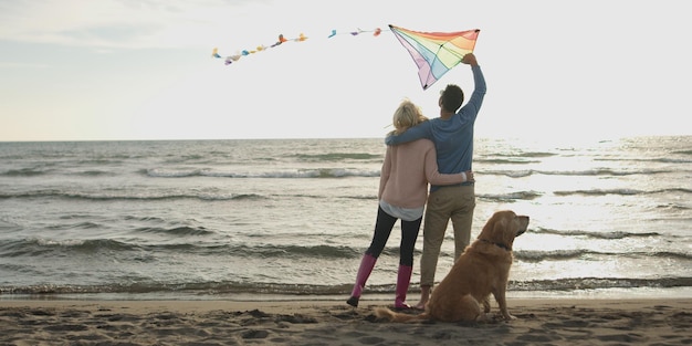 Pareja corriendo en la playa sosteniendo sus manos con perro el día del otoño