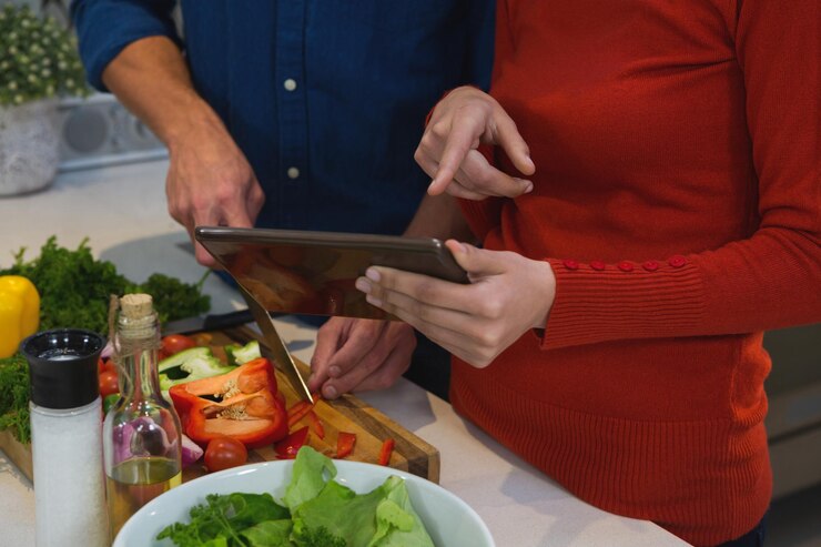 Foto una pareja cortando verduras mientras usa una tableta digital en la cocina de su casa