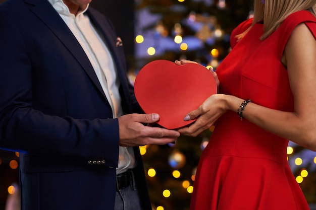 Pareja dando un regalo de Navidad delante de un árbol. Foto de alta calidad