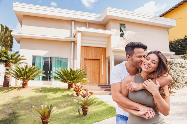 Foto pareja delante de la nueva casa grande y moderna, al aire libre feliz por el logro. pareja enamorada de la casa al fondo.