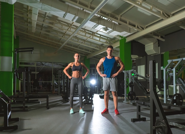 La pareja de deporte de pie en el moderno gimnasio en el fondo de luz brillante