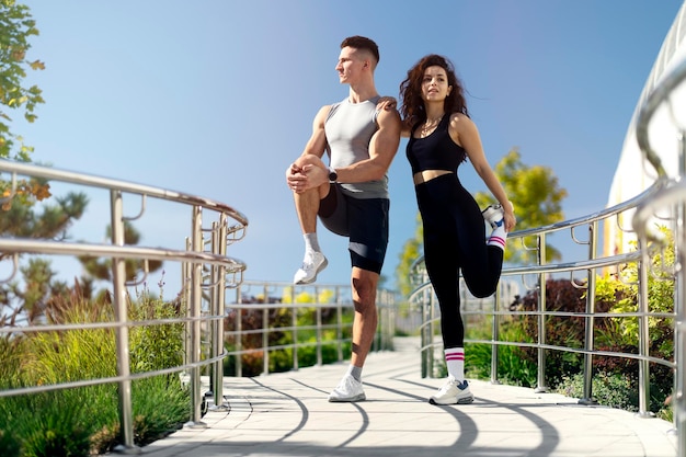 Pareja deportiva activa hombre y mujer estirando las piernas preparándose para correr