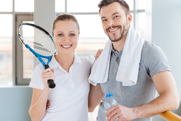 Pareja deportiva. Alegre joven pareja deportiva uniéndose entre sí y sonriendo mientras ambos están de pie en el club deportivo