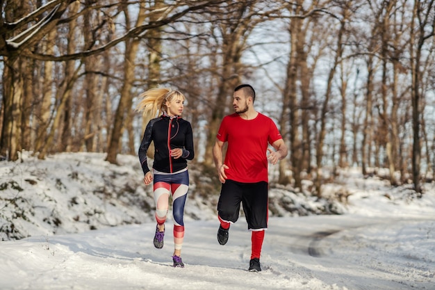 Pareja deportiva corriendo juntos en la naturaleza en el día de invierno cubierto de nieve. Relación, fitness de invierno, fitness al aire libre