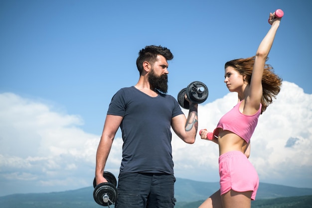 Pareja deportiva con mancuerna al aire libre Pareja haciendo ejercicio con pesas Hombre fuerte y mujer sexy haciendo ejercicio con pesas