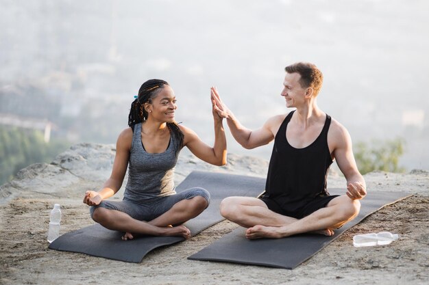 Pareja deportiva sentada en una alfombra de yoga y chocando los cinco