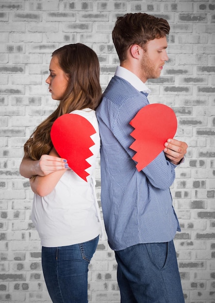 Pareja deprimida sosteniendo el corazón roto contra la pared de ladrillo