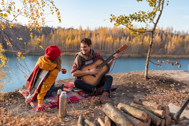 Una pareja descansa en la naturaleza contra el fondo de los árboles de otoño y el chico del río toca el