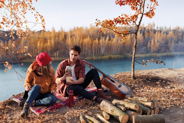 Una pareja descansa en la naturaleza contra el fondo de los árboles de otoño y el chico del río toca el