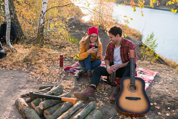 Una pareja descansa en la naturaleza contra el fondo de los árboles de otoño y el chico del río toca el