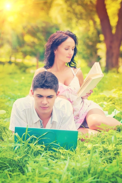 Pareja descansando con computadora portátil y libro en el parque en color de instagram de hierba