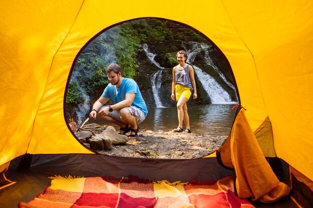 Pareja descansando en la playa del lago con vista a la cascada desde la carpa amarilla