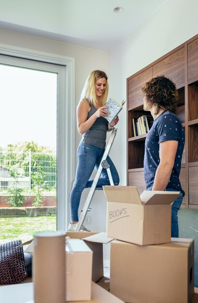 Pareja desempacando cajas de mudanza y colocando libros en el estante