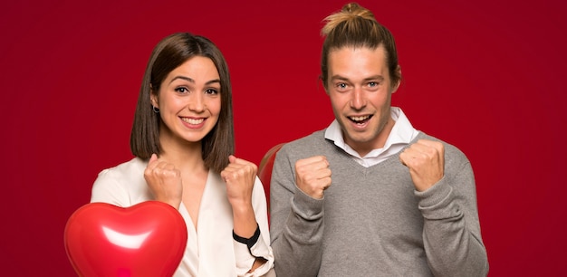 Pareja en el día de San Valentín celebrando una victoria en la posición de ganador sobre fondo rojo