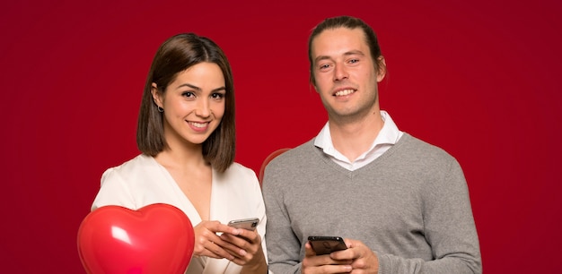 Pareja en el día de San Valentín enviando un mensaje con el móvil sobre fondo rojo