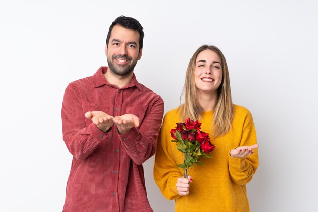 Pareja en el Día de San Valentín con flores sobre la pared aislada con copyspace imaginario en la palma para insertar un anuncio