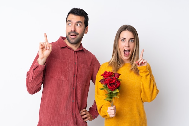 Pareja en el Día de San Valentín con flores sobre una pared aislada pensando una idea apuntando con el dedo