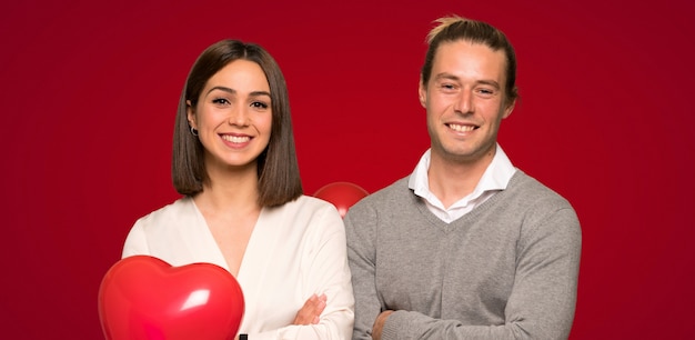 Pareja en el día de San Valentín que mantiene los brazos cruzados en posición frontal sobre fondo rojo