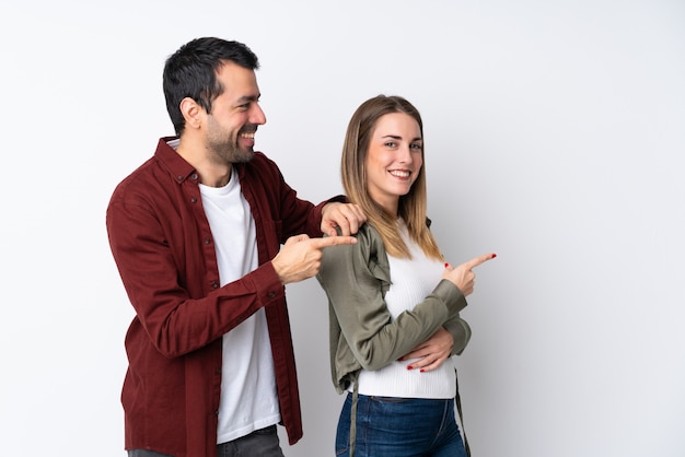 Pareja en el Día de San Valentín sobre la pared aislada que señala el dedo hacia un lado y presenta un producto