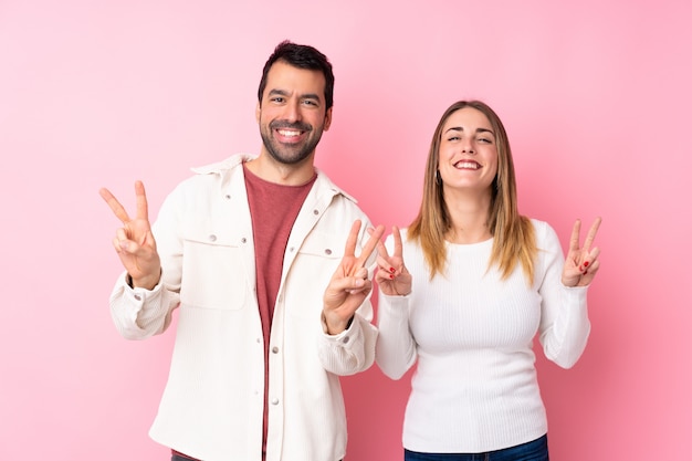 Pareja en el Día de San Valentín sobre pared rosa aislado sonriendo y mostrando el signo de la victoria con ambas manos