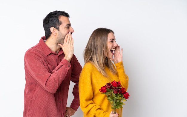 Pareja en el Día de San Valentín sosteniendo flores sobre pared aislada gritando con la boca abierta al lateral