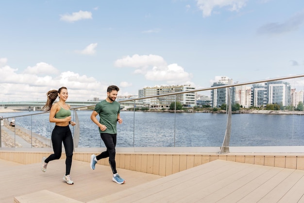 Una pareja disfruta de una carrera junto al río en un día soleado, mezclando el ejercicio con el entorno urbano frente al mar.