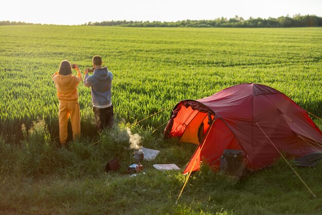 Pareja disfruta de la vista del atardecer en el campamento en campo verde