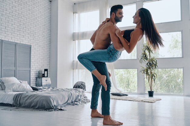 Pareja disfrutando bailando. Longitud total de la hermosa joven pareja abrazándose y sonriendo mientras baila en el dormitorio