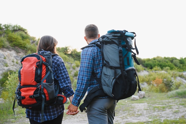 Pareja disfrutando de hermosas vistas a las montañas, mientras viaja con mochilas en las montañas