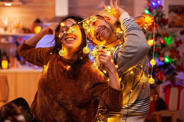 Pareja divertida caughting en la luz del árbol de Navidad durante la época navideña