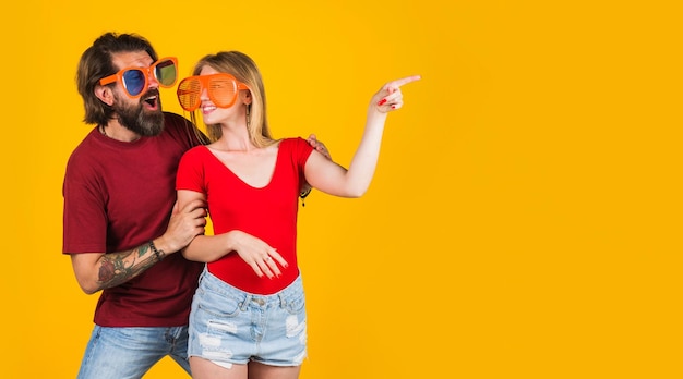 Foto pareja divertida en gafas grandes y camiseta roja mujer sonriente señalando el espacio de la copia con la chica del dedo