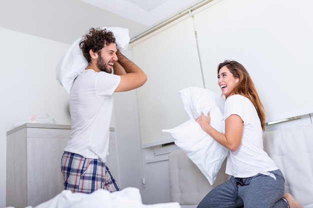 Pareja divirtiéndose mientras pelea de almohadas. Joven pareja feliz golpeó las almohadas de la cama en un dormitorio en casa.