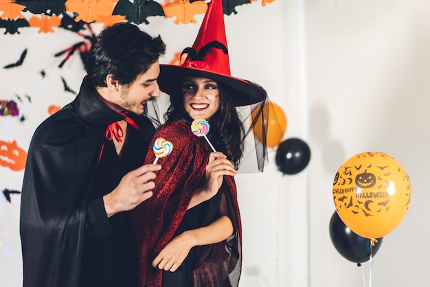 Pareja divirtiéndose sosteniendo calabazas y vistiendo disfraces de carnaval vestidos de halloween