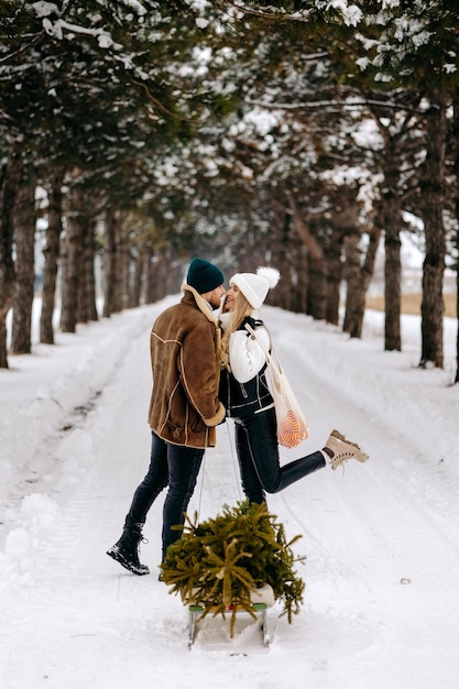 Una pareja divirtiéndose con trineo en un bosque de árboles de Navidad, comiendo mandarinas y disfrutando de un nevado