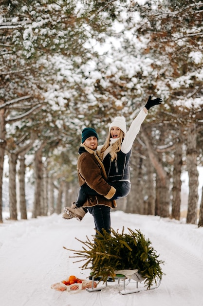 Una pareja divirtiéndose con trineo en un bosque de árboles de Navidad, comiendo mandarinas y disfrutando de un nevado