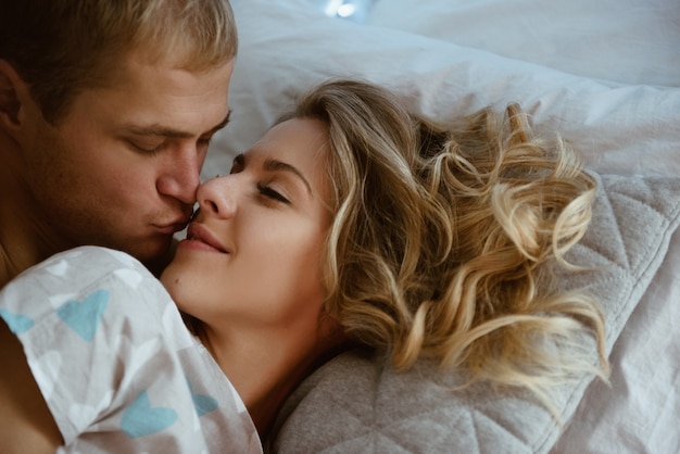 Pareja en el dormitorio en la cama en el dormitorio. Una chica rubia en pijama, un chico con el torso desnudo. Tiempo de Navidad.