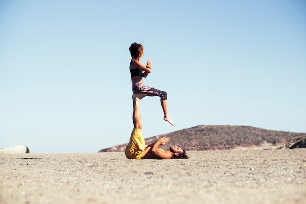 Pareja de dos adultos en relación o amistad haciendo acro yoga juntos - hombre sosteniendo con sus piernas a una mujer mientras ella está sentada