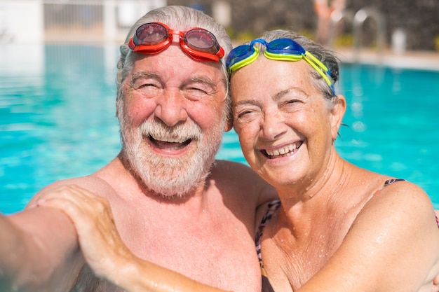 Pareja de dos ancianos felices divirtiéndose y disfrutando juntos en la piscina tomando una foto selfie sonriendo y mirando a la cámara. Gente feliz disfrutando del verano al aire libre en el agua