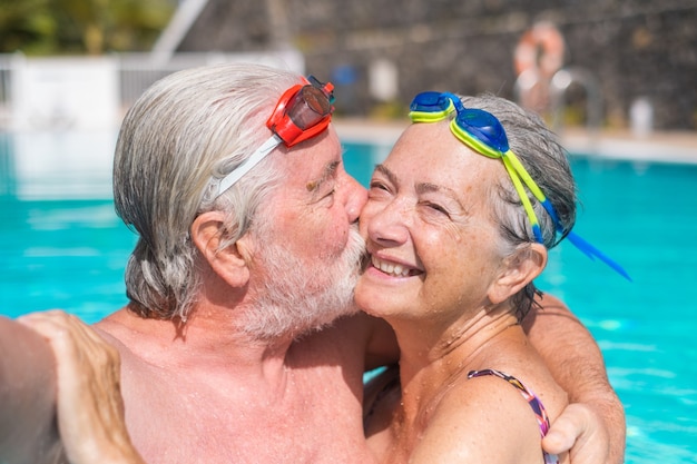 Pareja de dos ancianos felices divirtiéndose y disfrutando juntos en la piscina tomando una foto selfie sonriendo y mirando a la cámara. Gente feliz disfrutando del verano al aire libre en el agua