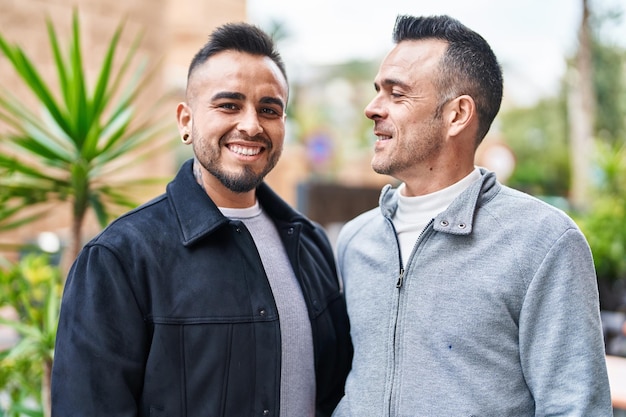 Pareja de dos hombres sonriendo seguros de pie juntos en la calle