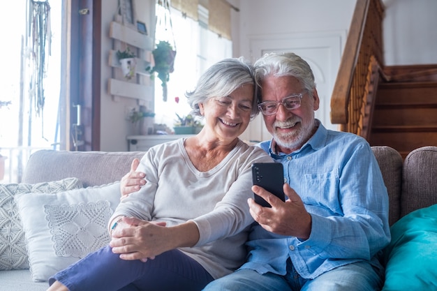 Pareja de dos personas mayores y maduras en casa con tableta juntos en el sofá. Portátil de uso senior divirtiéndose y disfrutando mirándolo. Concepto de ocio y tiempo libre.