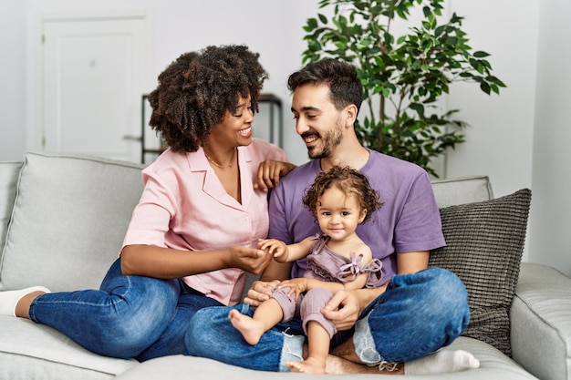 Pareja e hija sonriendo confiados sentados en el sofá en casa