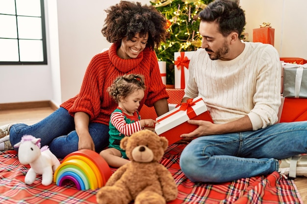 Pareja e hija sosteniendo un regalo sentado junto al árbol de Navidad en casa