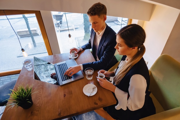 Una pareja elegante toma café por la mañana en la cafetería y trabaja con una computadora portátil