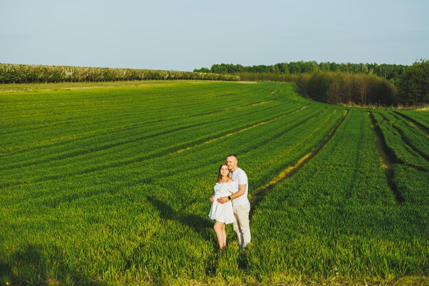 Pareja embarazada abrazándose en un campo verde de primavera Futuros padres en el parque de árboles con flores blancas Una pareja romántica esperando un bebé Un paseo por un campo verde