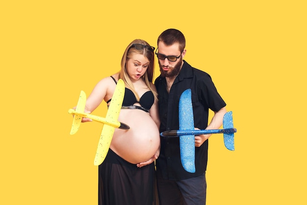 Pareja embarazada divertirse jugando con aviones sobre fondo amarillo