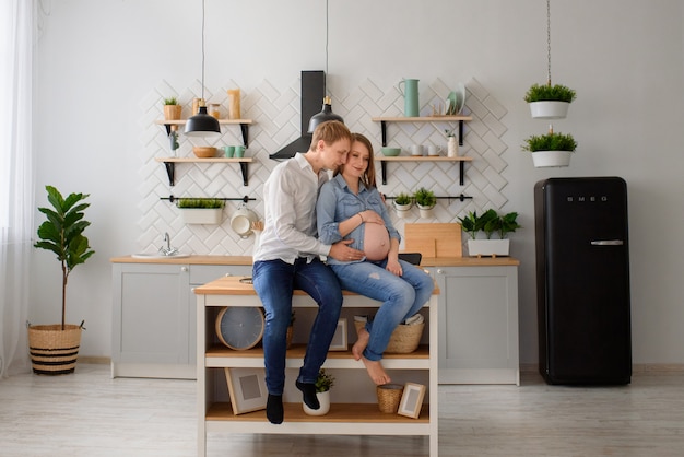 Pareja embarazada enamorada sentada en la cocina