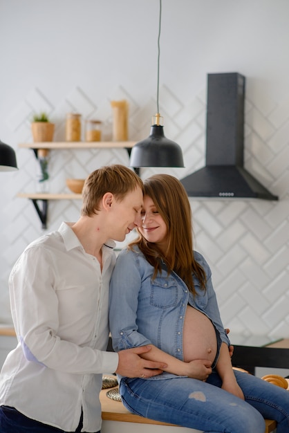 Pareja embarazada enamorada sentada en la cocina