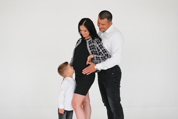 Una pareja embarazada, una familia joven con un hijo pequeño, se para en un fondo gris riéndose y esperando a su hijo por nacer