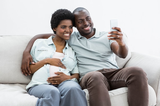 Pareja embarazada tomando una selfie en teléfono móvil en casa